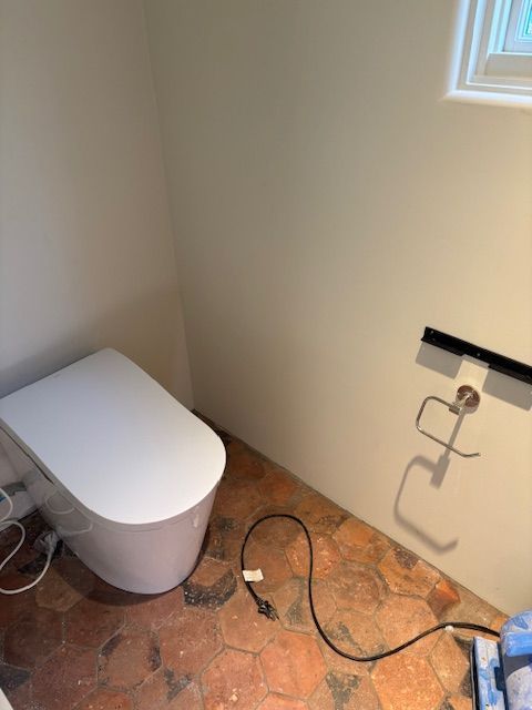 Modern white toilet in a bathroom with brown tile floor and white walls.