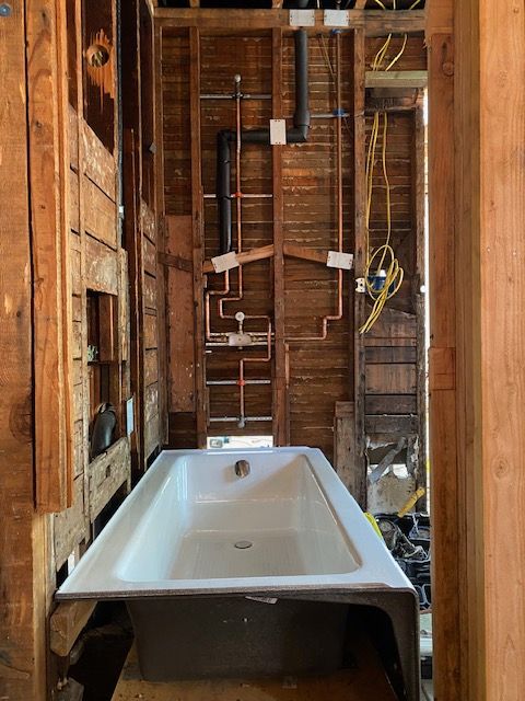 Bathtub installed in a framed-out bathroom with exposed plumbing and electrical wiring.