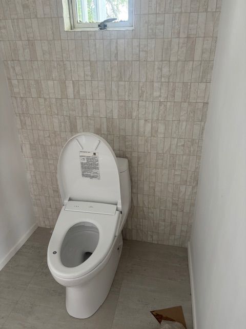A white toilet with the seat up in a small bathroom. Walls are light-colored tile.