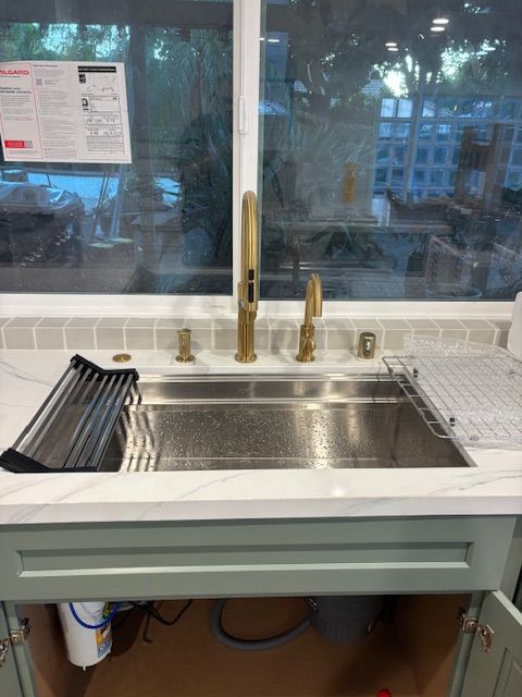 Gold faucet and sink in a kitchen, with a window and white countertop.