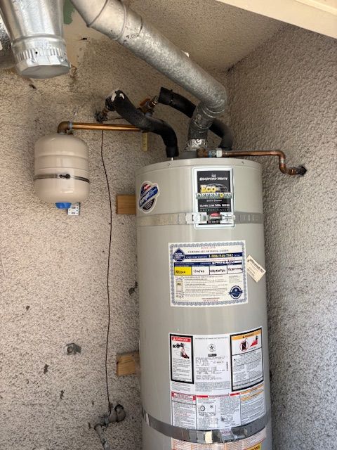 Water heater with an expansion tank, pipes, and vent. Set in a stucco enclosure.