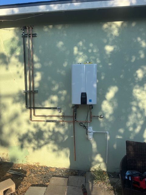 Gas water heater mounted on a light green wall with copper pipes. Sunlight and shadows.