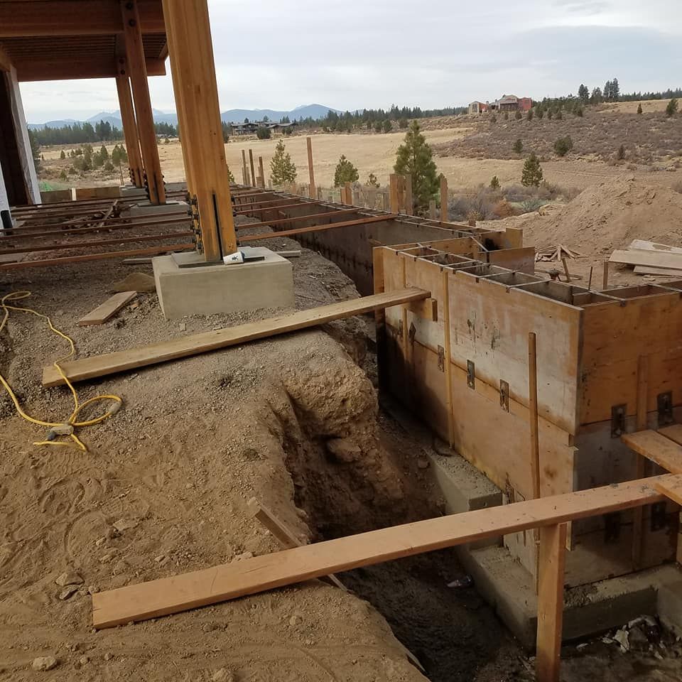 Construction site with wooden forms for a curved foundation, dirt and landscape in background.