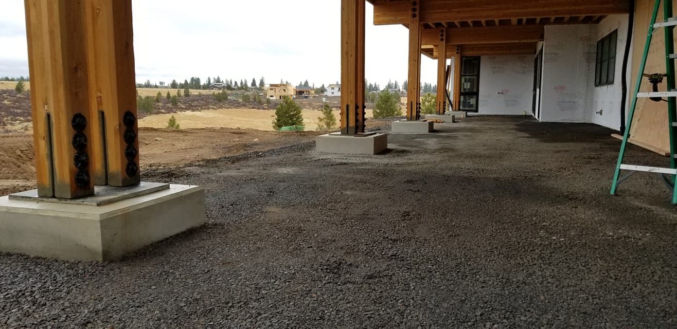 Wooden beams supporting a porch, gravel ground, overlooking a landscape.