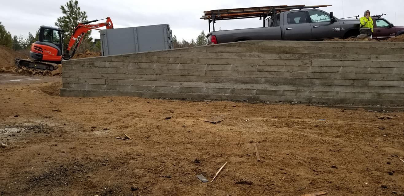 An excavator working at a construction site with a truck and a person in the background.