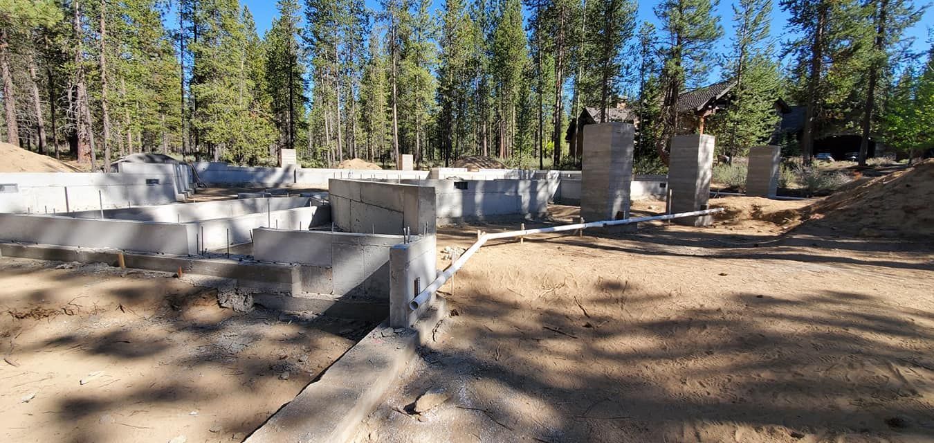 Concrete foundation under construction in a wooded area on a sunny day.