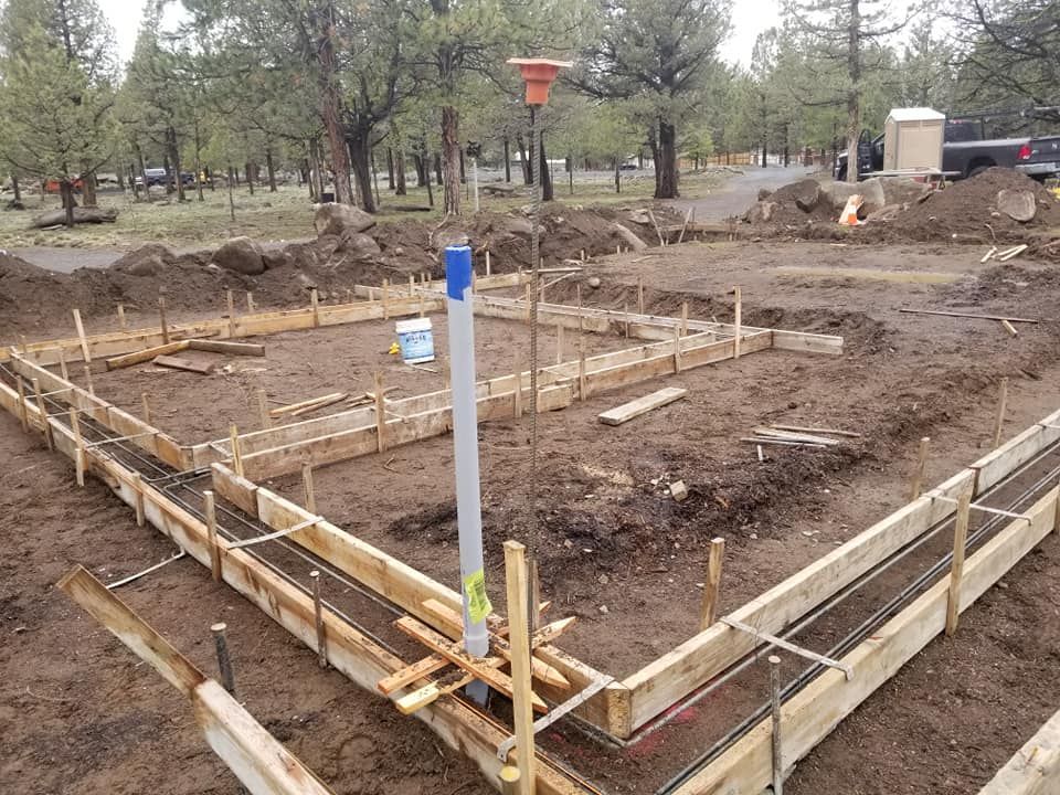 Construction site with wooden forms, rebar, and a vertical pipe, ready for a concrete foundation.