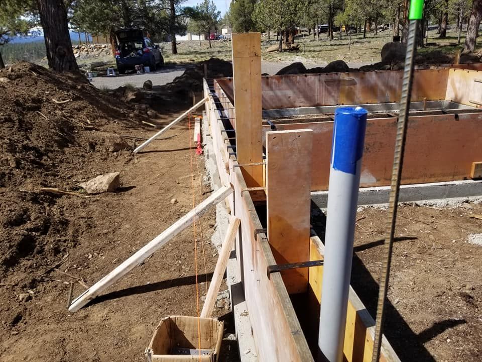 Construction site with wooden forms for a concrete foundation, dirt, and a PVC pipe in place.