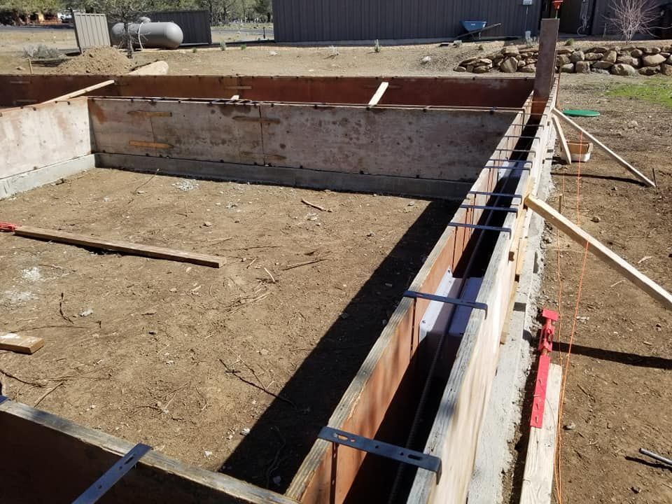 Wooden forms for a concrete foundation, outdoors on a dirt ground.