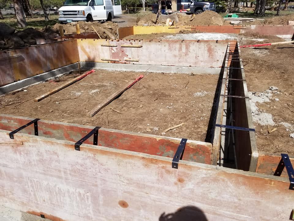 Construction site with wooden forms for a concrete foundation, soil fill. White van and trucks in the background.