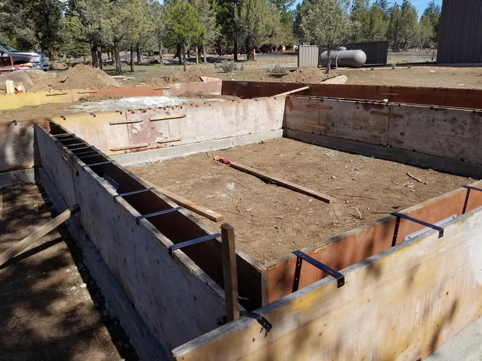 Wooden forms hold a foundation awaiting concrete pour. Rebar is visible. Outdoors.