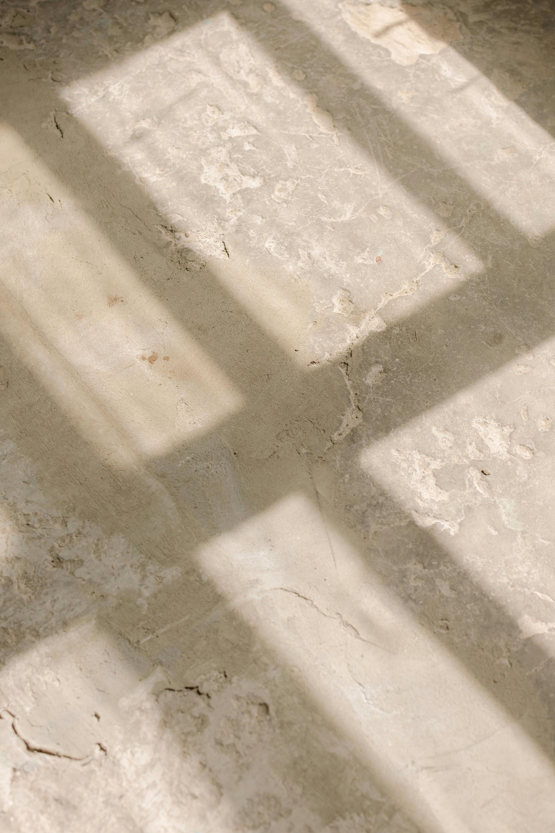 Shadow of a window frame on a textured, light-colored floor.