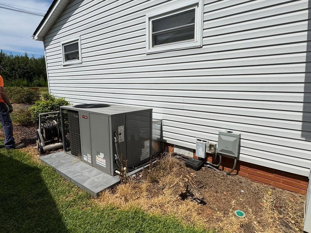 HVAC unit on a concrete pad next to a house with white siding, grass, and a person.