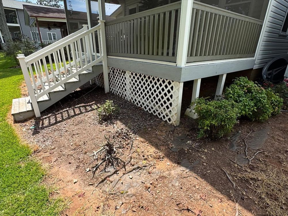 Wooden deck with white lattice skirting and stairs over a dirt and mulch bed.