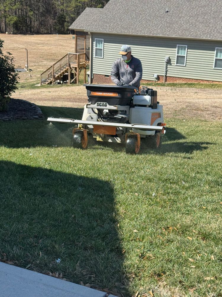 Person operating a commercial lawn spreader on a lawn, applying product to the grass.