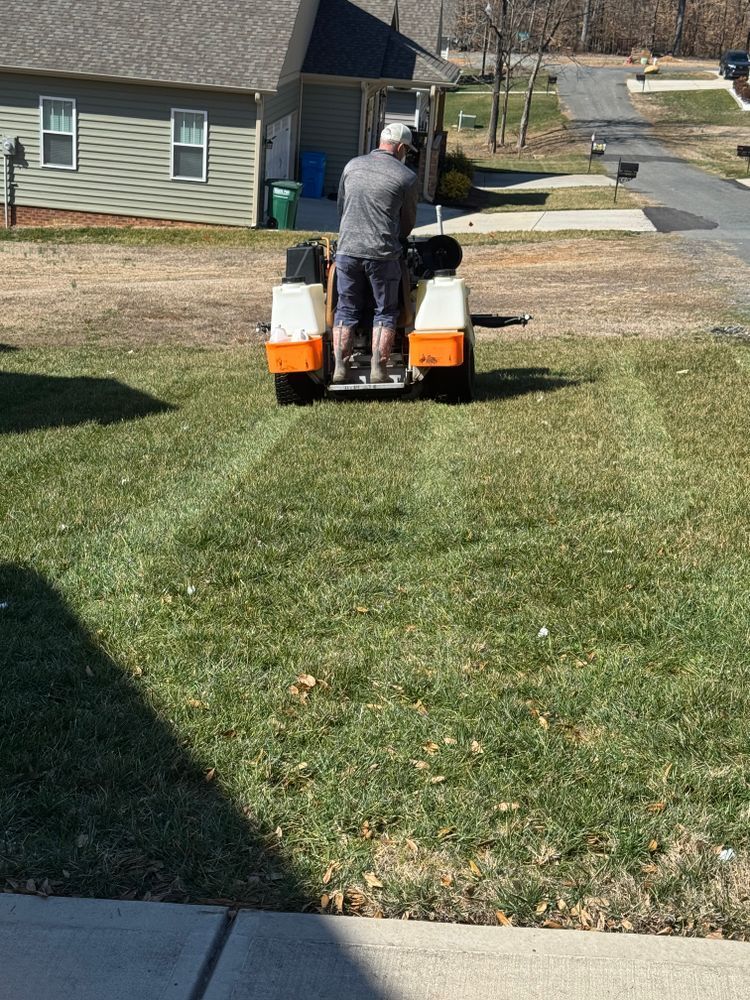 Person on a small riding lawnmower mowing a grassy lawn in front of a house on a sunny day.