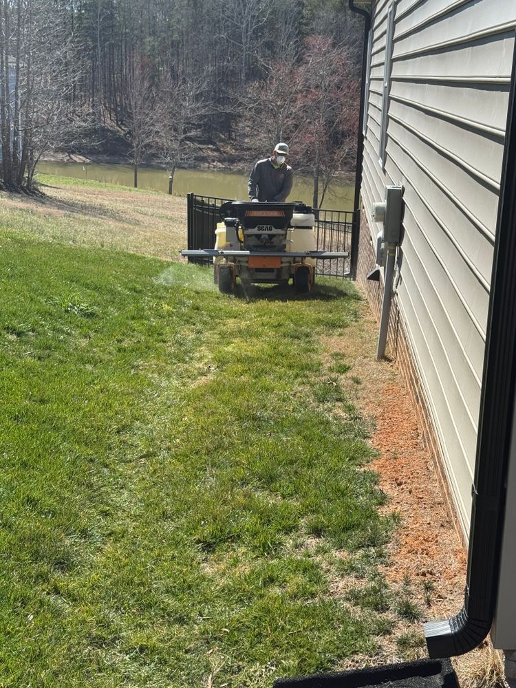 Man on riding lawnmower cutting grass next to house. Green lawn, brown soil edge.