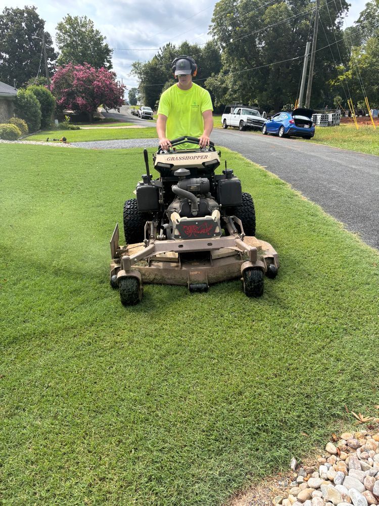 Man mowing a lawn with a riding mower on a sunny day.