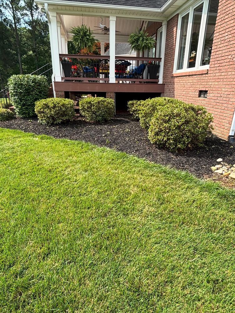 A house exterior with a porch, green lawn, and shrubbery along a dark mulch bed.