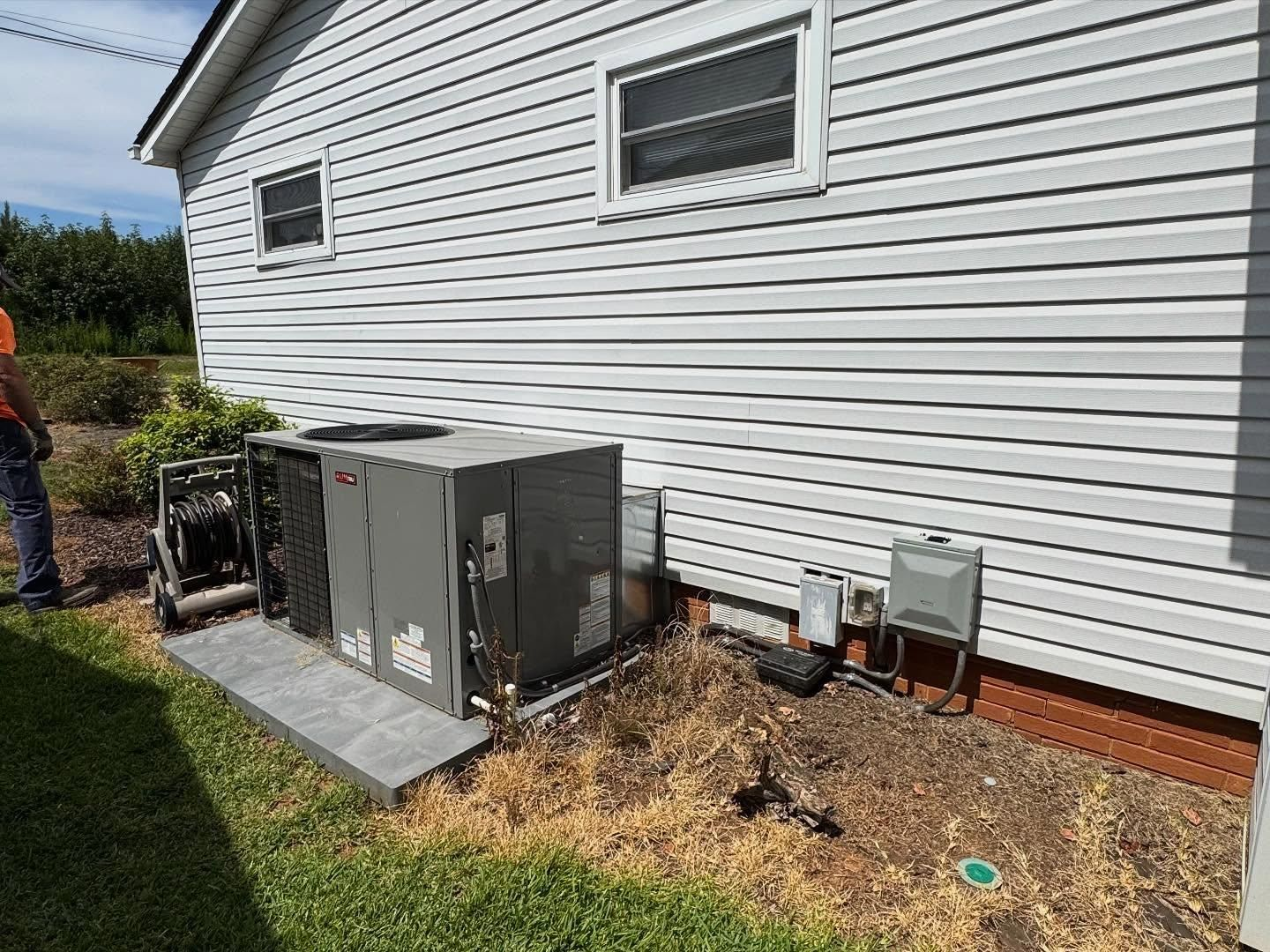 HVAC unit beside a house with white siding and a grassy yard. A person stands nearby.