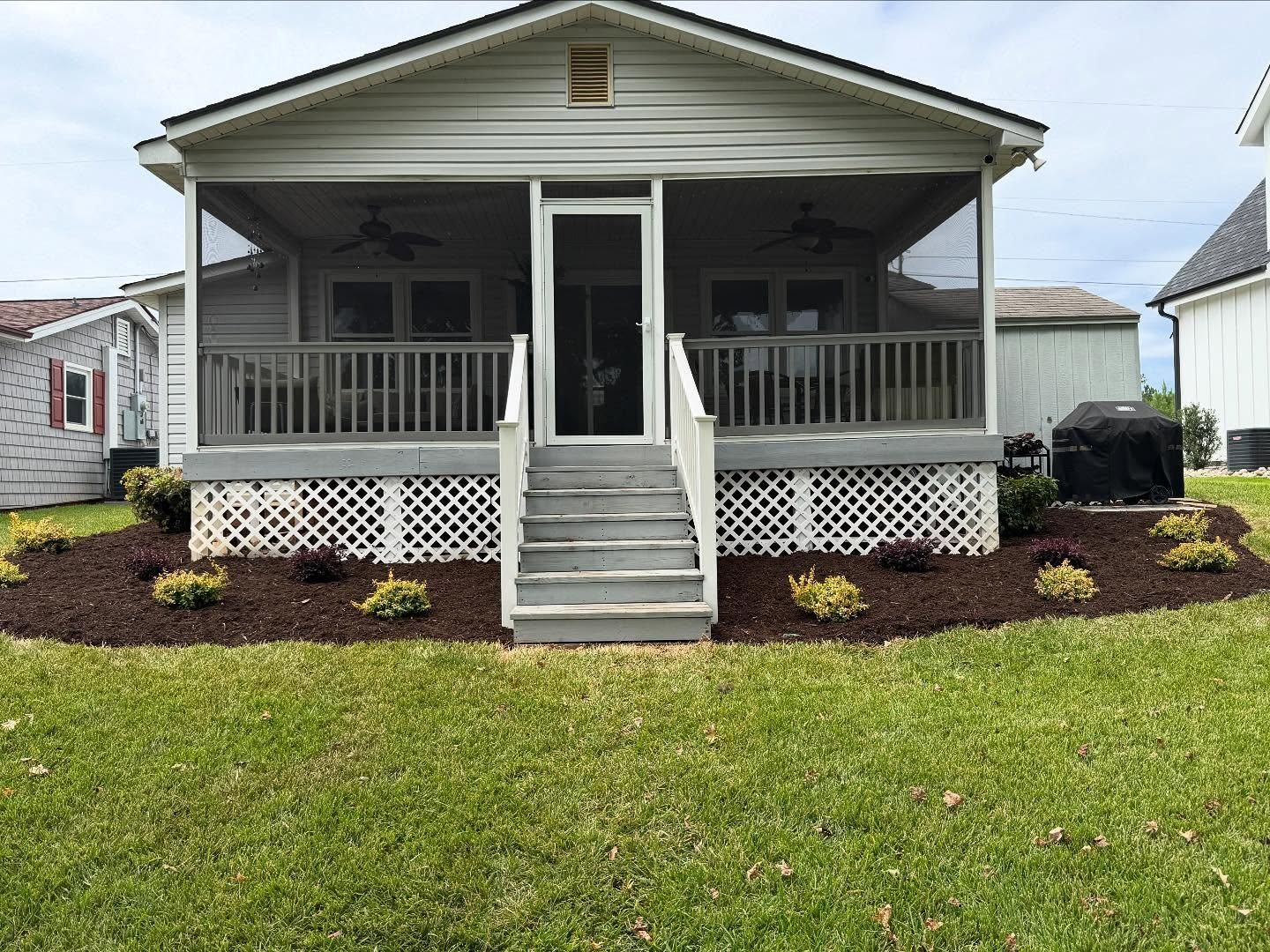 Cottage with screened porch, gray siding, white lattice, wooden steps, and landscaped bed.