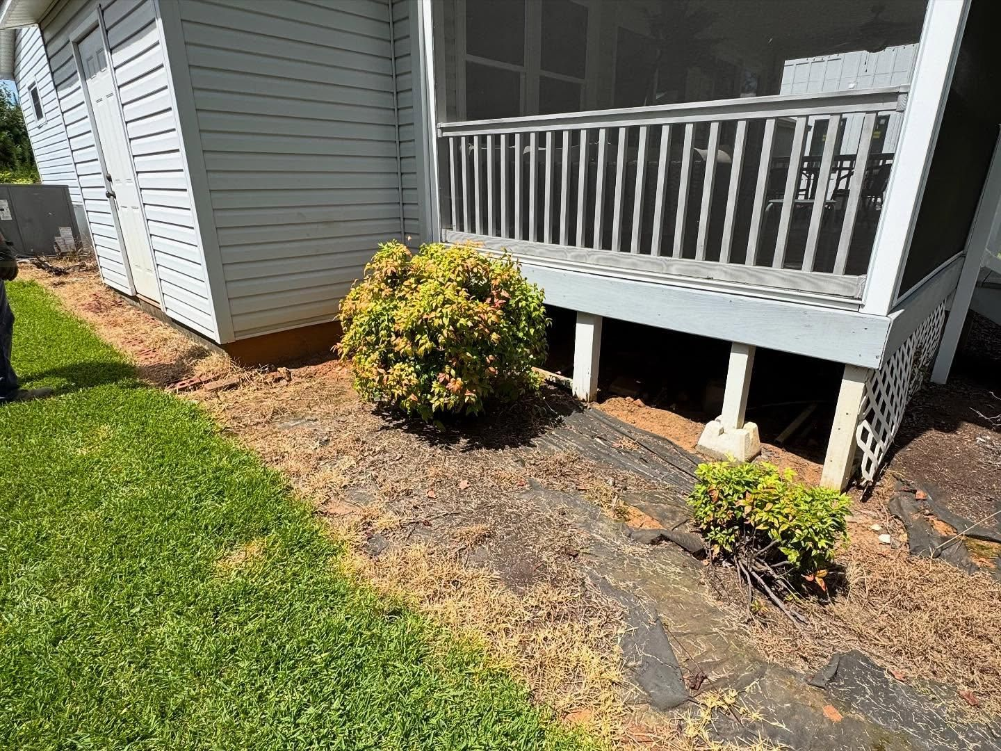A house with a small porch, featuring a bush and garden bed with mulch. Green grass is to the left.