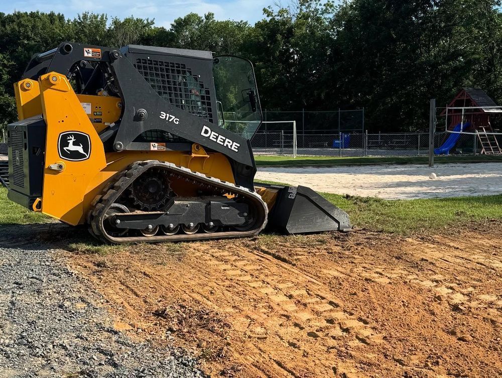 Yellow John Deere skid steer on dirt near a playground.