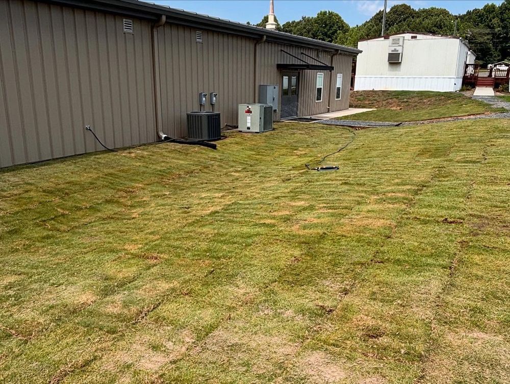 Exterior view of building with patches of grass and HVAC units, with a white trailer in the background.