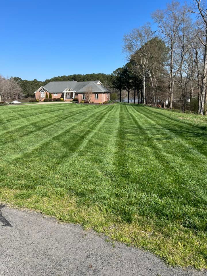 Lawn with mowing stripes in front of a brick house under a blue sky.