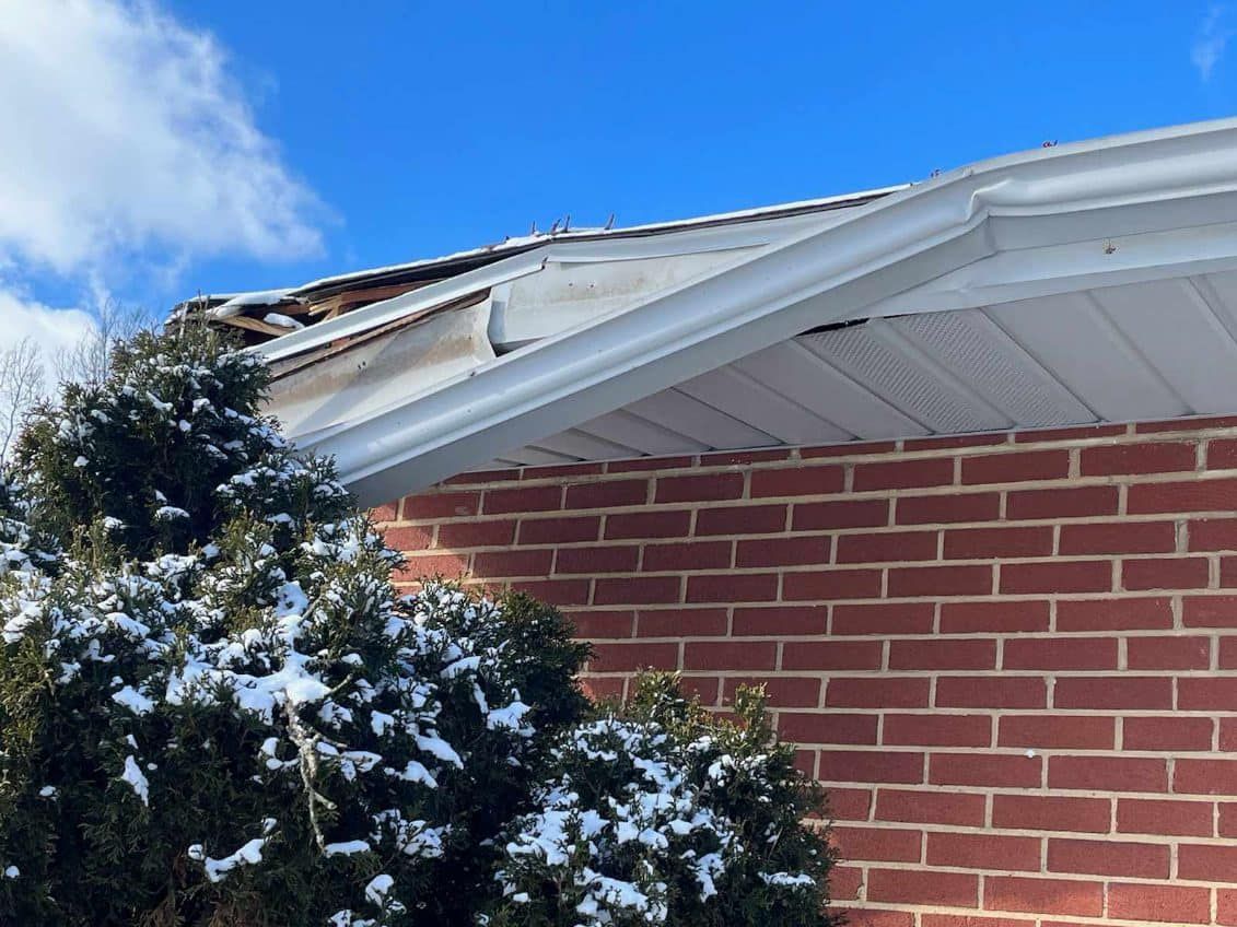 A brick house with a roof that has been damaged by a tree.