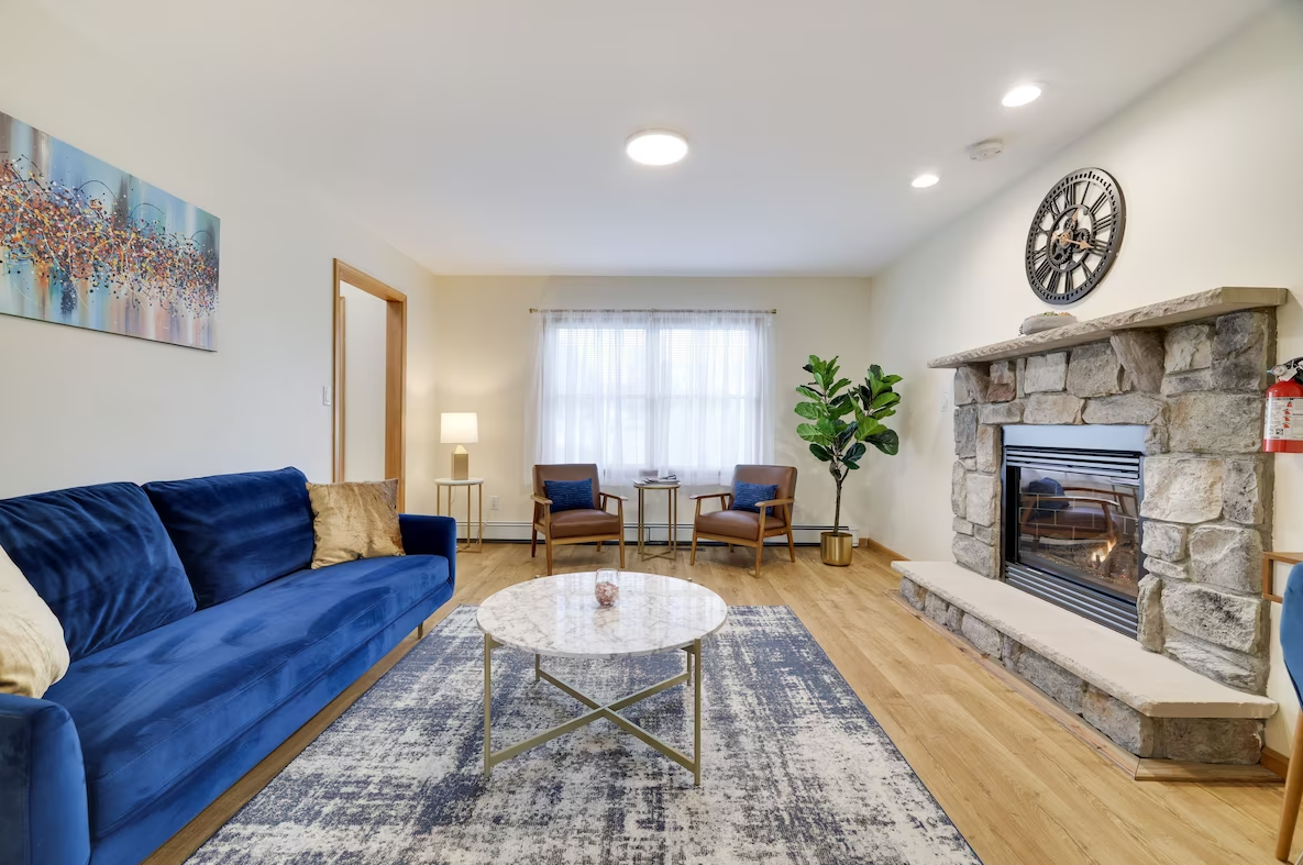A living room with a blue couch , a lamp , and a painting on the wall.