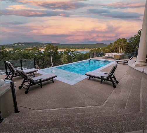 Pool with lounge chairs overlooking a lake at sunset.