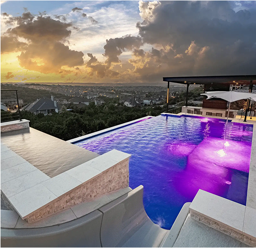 Rooftop pool with purple lights, overlooking a city at sunset.