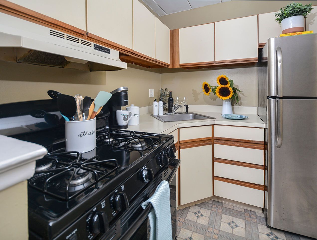 Compact apartment kitchen with gas range, sink, and a stainless steel refrigerator.