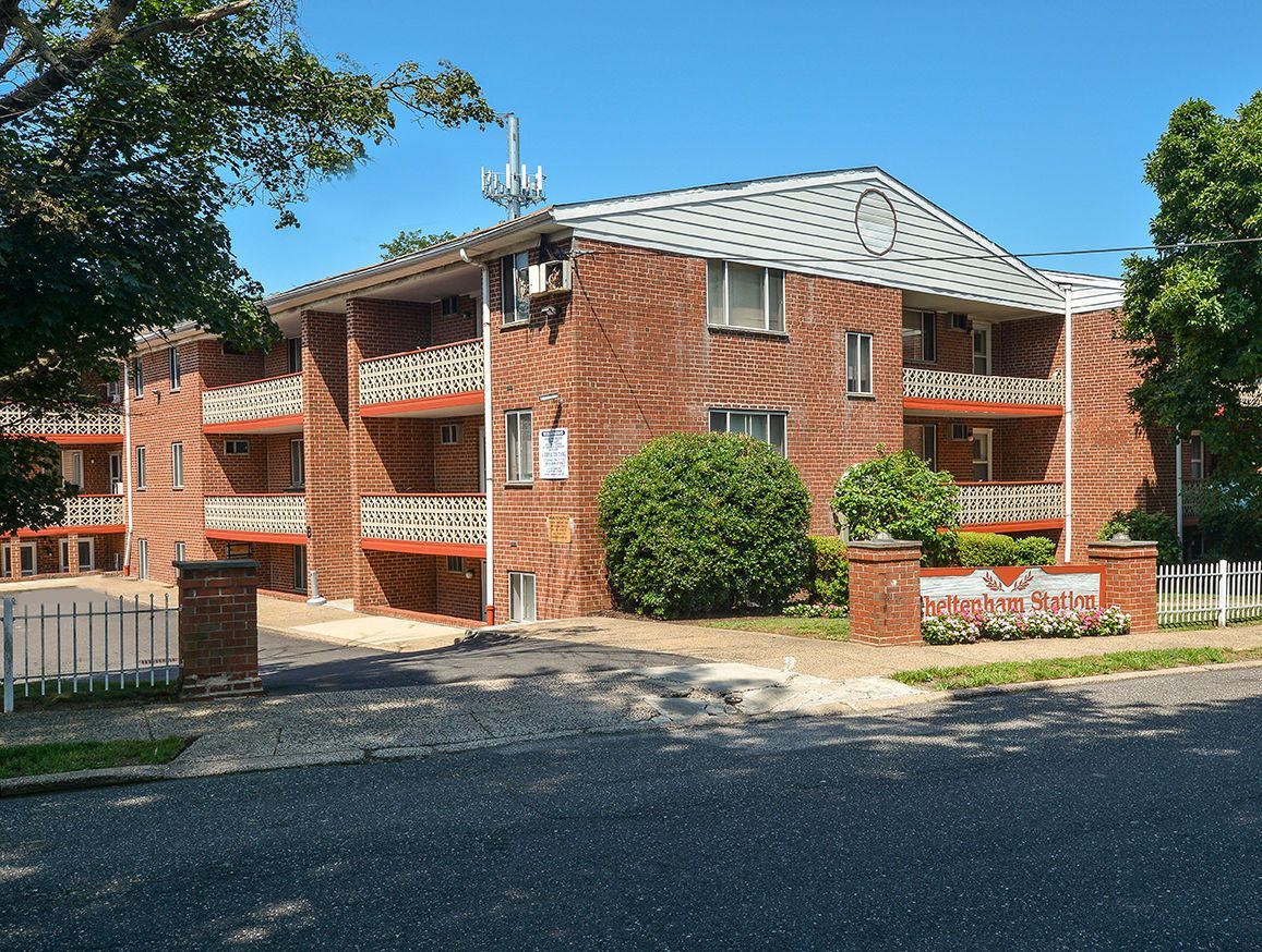 Exterior view of a brick apartment building with balconies and a landscaped entry sign.