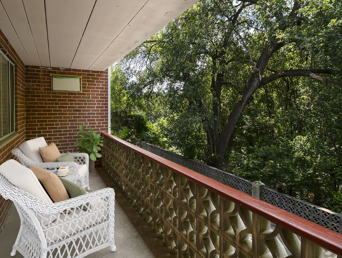 Balcony with white wicker chairs and cushions, overlooking trees.
