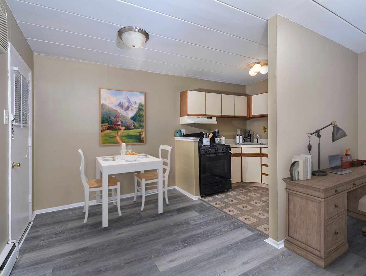 Dining area with a white table and chairs beside a compact kitchen with beige walls.
