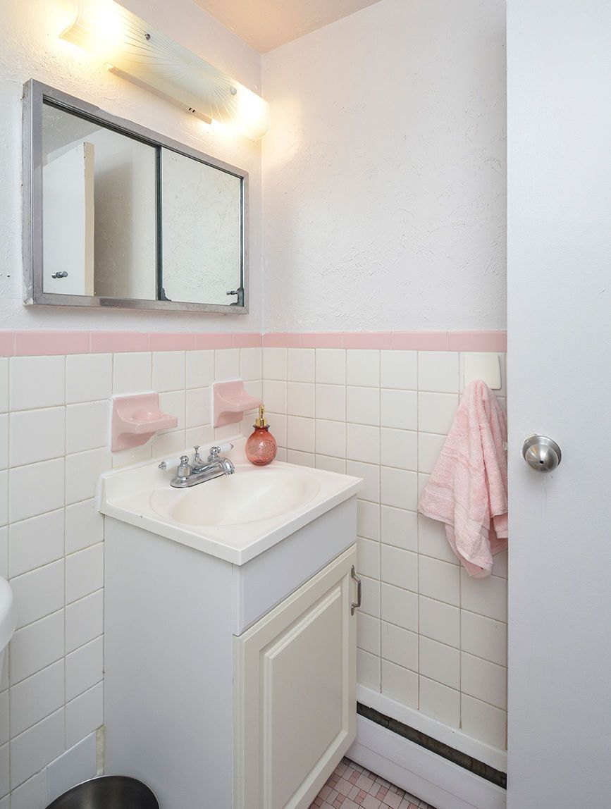 Small apartment bathroom vanity with sink, mirror, and pink-tiled walls.