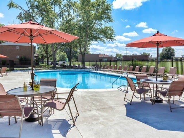 Outdoor community pool with lounge chairs, tables, and pink umbrellas.
