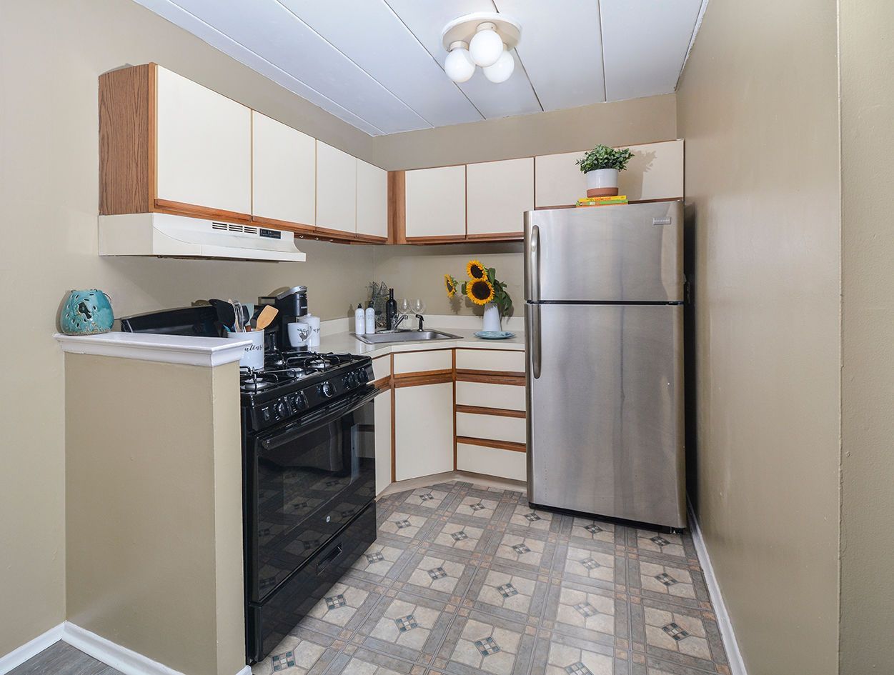 Compact apartment kitchen with beige walls, white upper cabinets, and a stainless steel refrigerator.