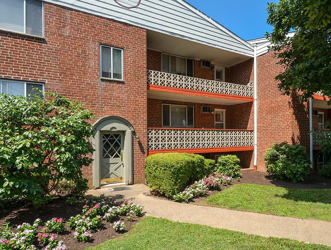 Exterior of a brick apartment building with balconies and landscaped walkway.
