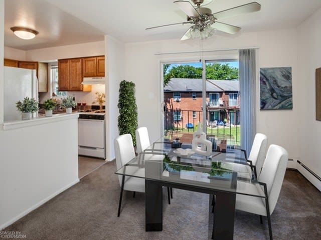 Dining area in an apartment with a glass table, white chairs, and a view of the courtyard through a sliding glass door.