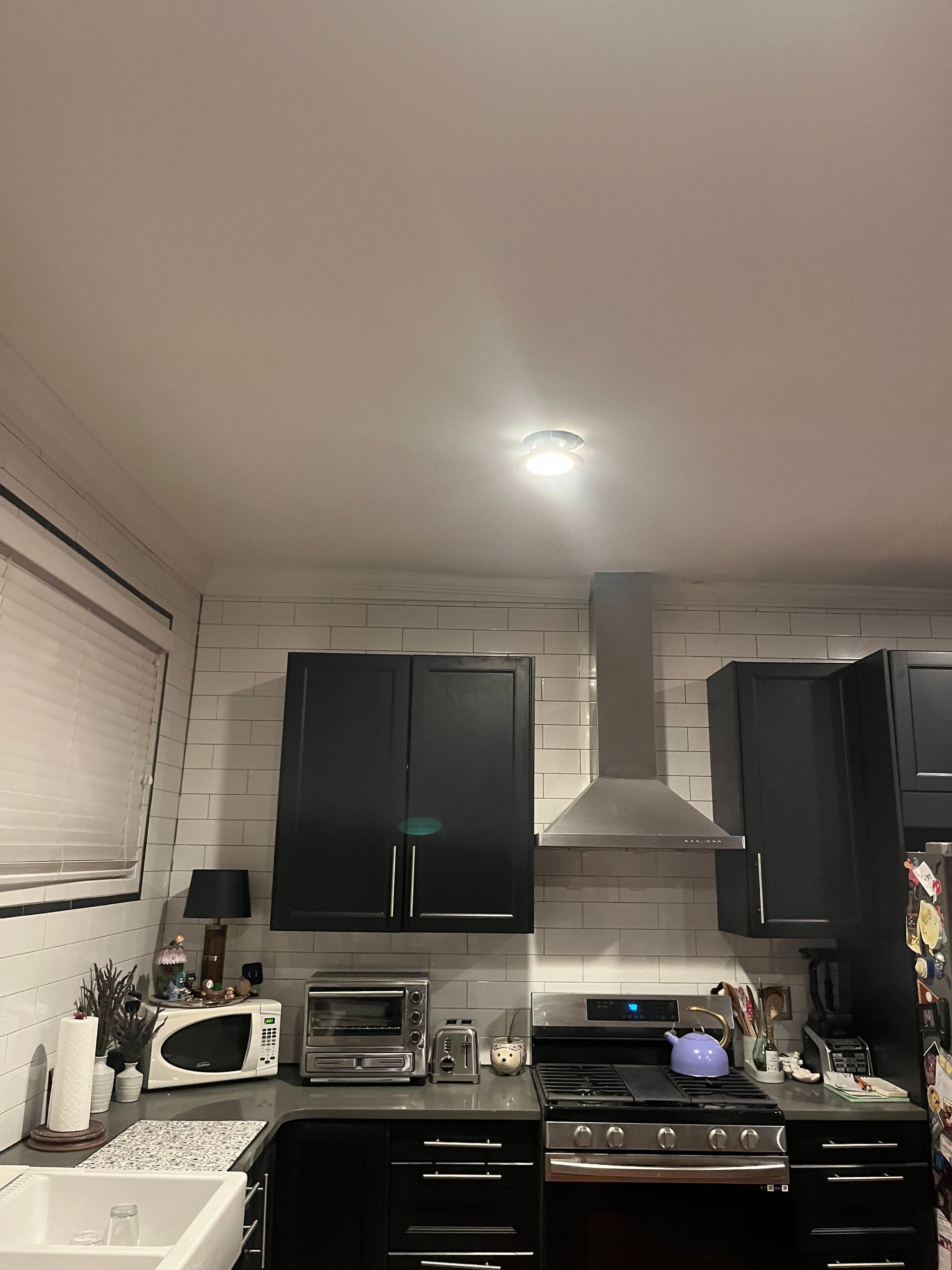 A kitchen with black cabinets , a stove , a sink , and a microwave.
