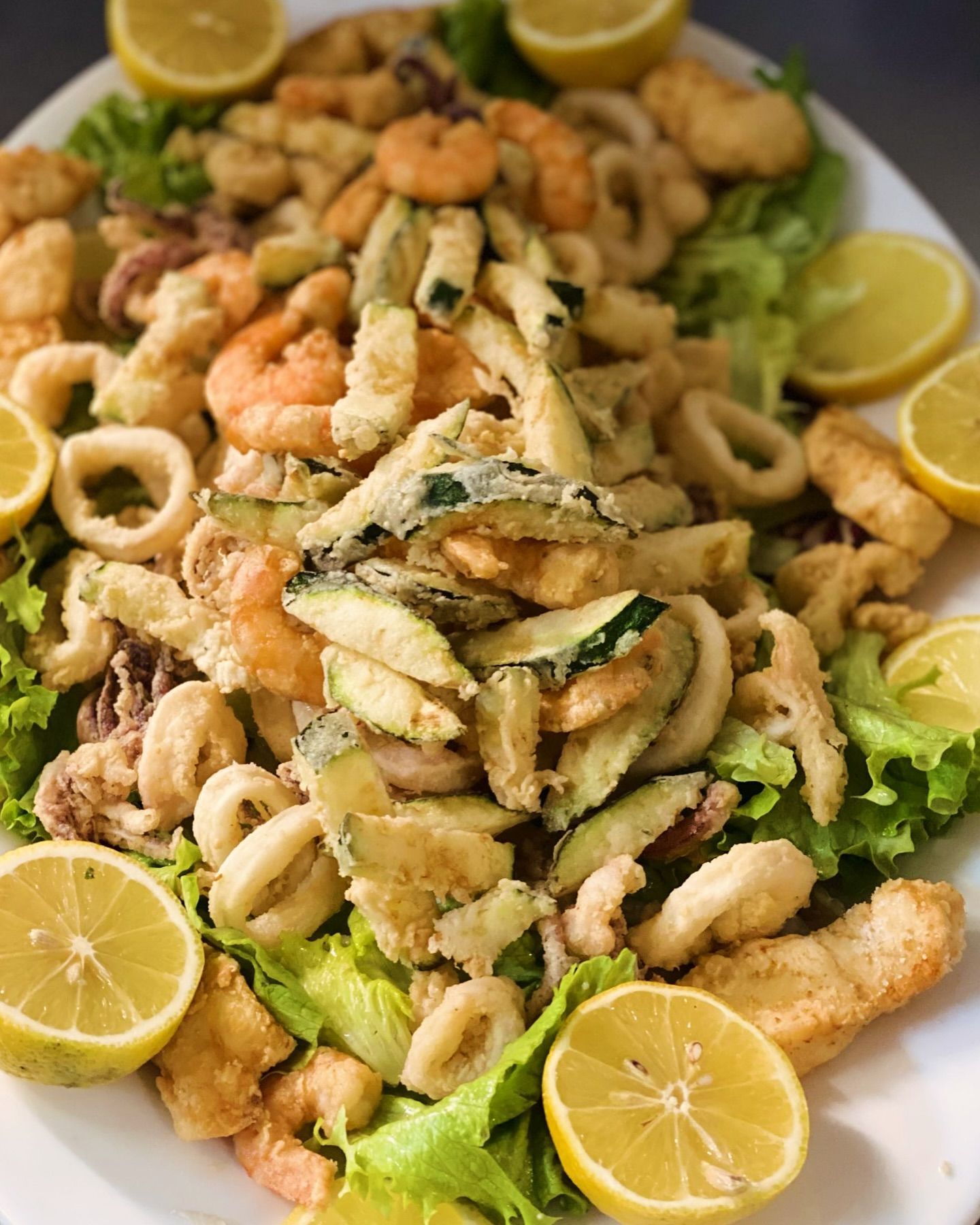 Frutti di mare fritti e zucchine con fette di limone su un letto di lattuga.