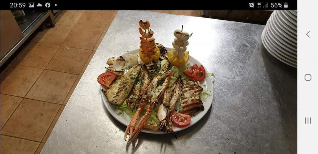 Piatto di frutti di mare alla griglia, tra cui gamberi, scampi e spiedini, servito su una superficie metallica.