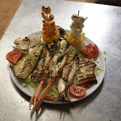 Piatto di pesce alla griglia con gamberi, scampi, pesce e verdure su un piatto bianco.