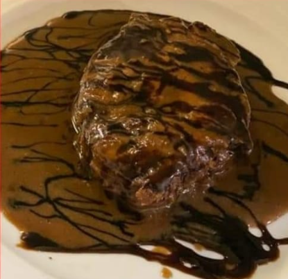 Manzo alla Wellington in salsa marrone, condito con una salsa più scura, su un piatto bianco.