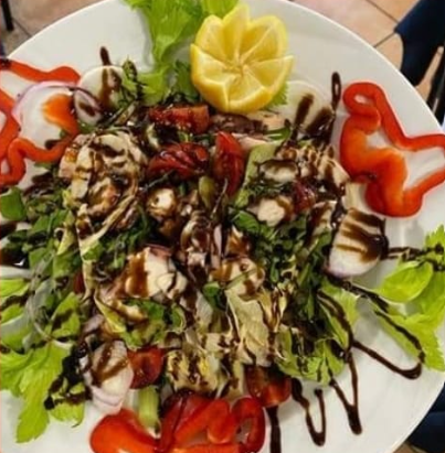 Insalata con lattuga, pomodori, formaggio, peperoni, limone e glassa balsamica su un piatto bianco.