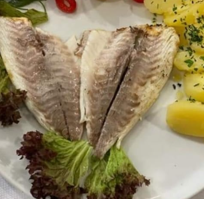 Filetti di pesce alla griglia su un piatto bianco con lattuga e patate.