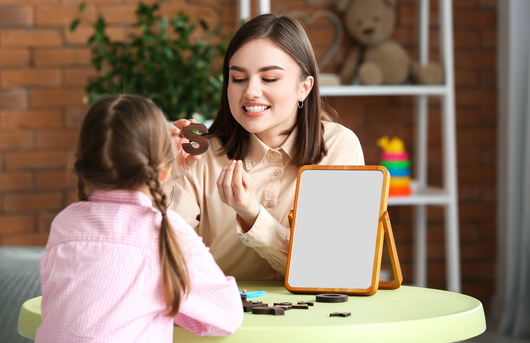 A speech therapist shows a child a letter to practice articulation skills at a table.